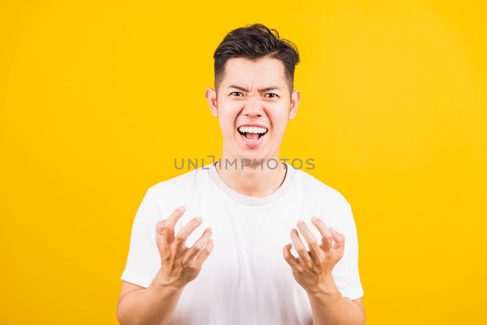 Portrait Aaian handsome young man standing wearing white t-shirt he expressions irate, angry face screaming, studio shot isolated yellow background