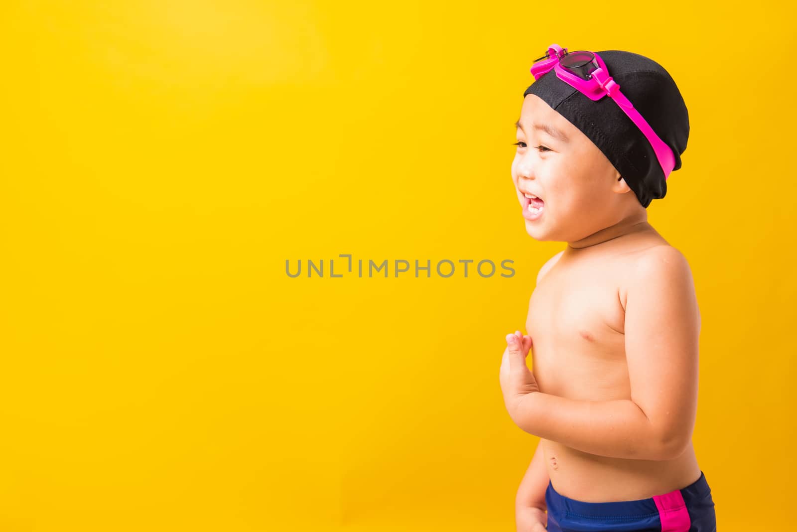 Summer vacation concept, Closeup portrait Asian happy cute little child boy wearing goggles and swimsuit, Kid having fun with in summer vacation looking side, studio shot isolated yellow background