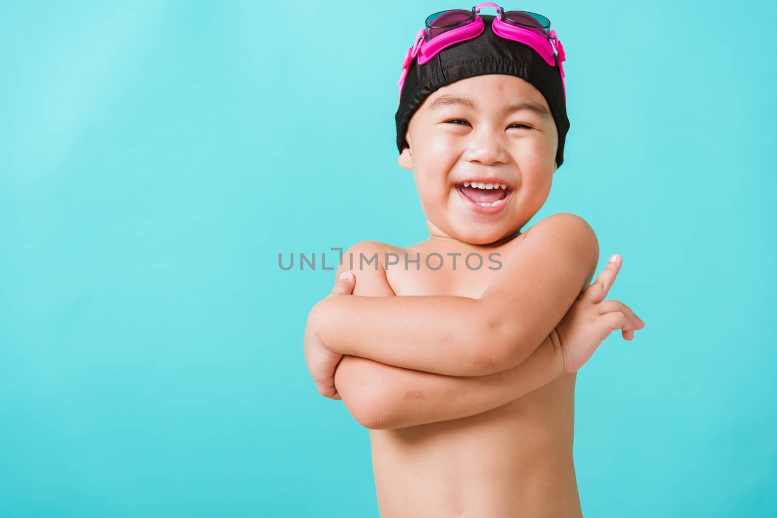 Summer vacation concept, Closeup portrait Asian happy cute little child boy wear goggles and swimsuit, Kid having fun with in summer vacation crossed arm, studio shot isolated blue background