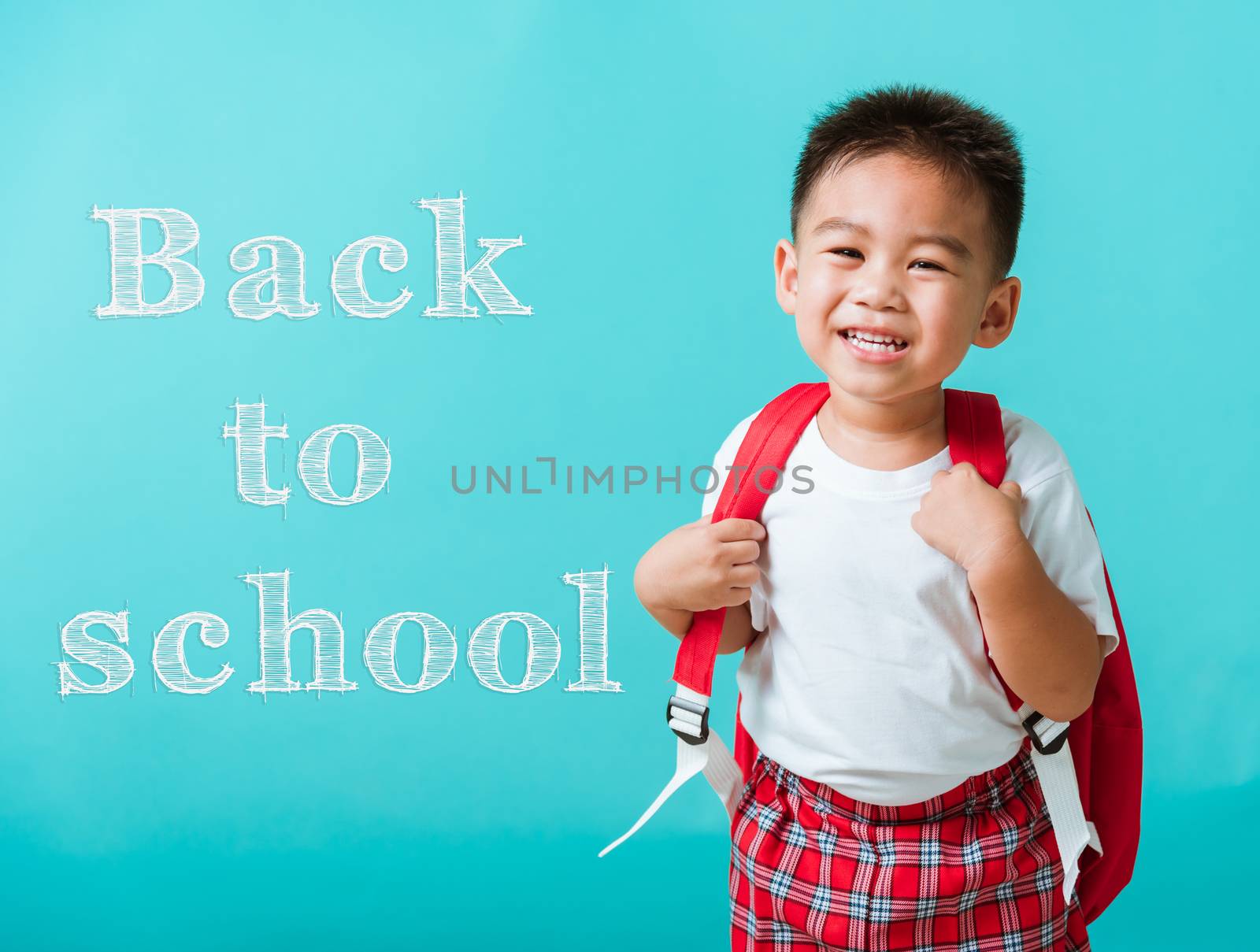 Back to school concept. Portrait closeup happy Asian cute little child boy in uniform smiling, isolated blue background. The kid from preschool kindergarten with a school bag backpack