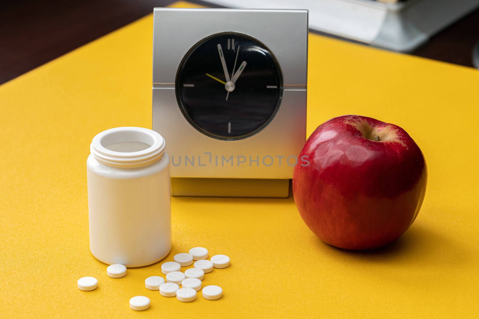 A colorful set of grey alarm clock, red Apple and pill bottles on a bright light yellow background. Medicine of creative concepts. Minimal style with a colorful paper background.