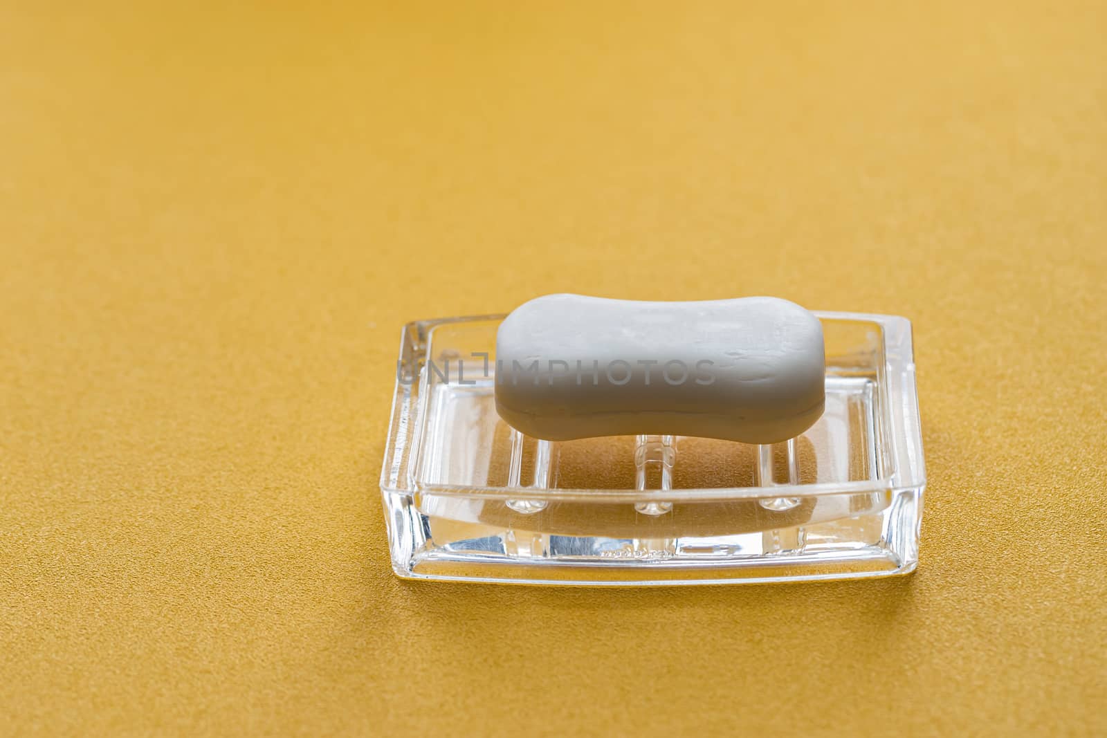 A piece of white soap on a transparent stand on a yellow background. Protect against the coronavirus. Coronavirus pandemic protection by washing hands frequently.