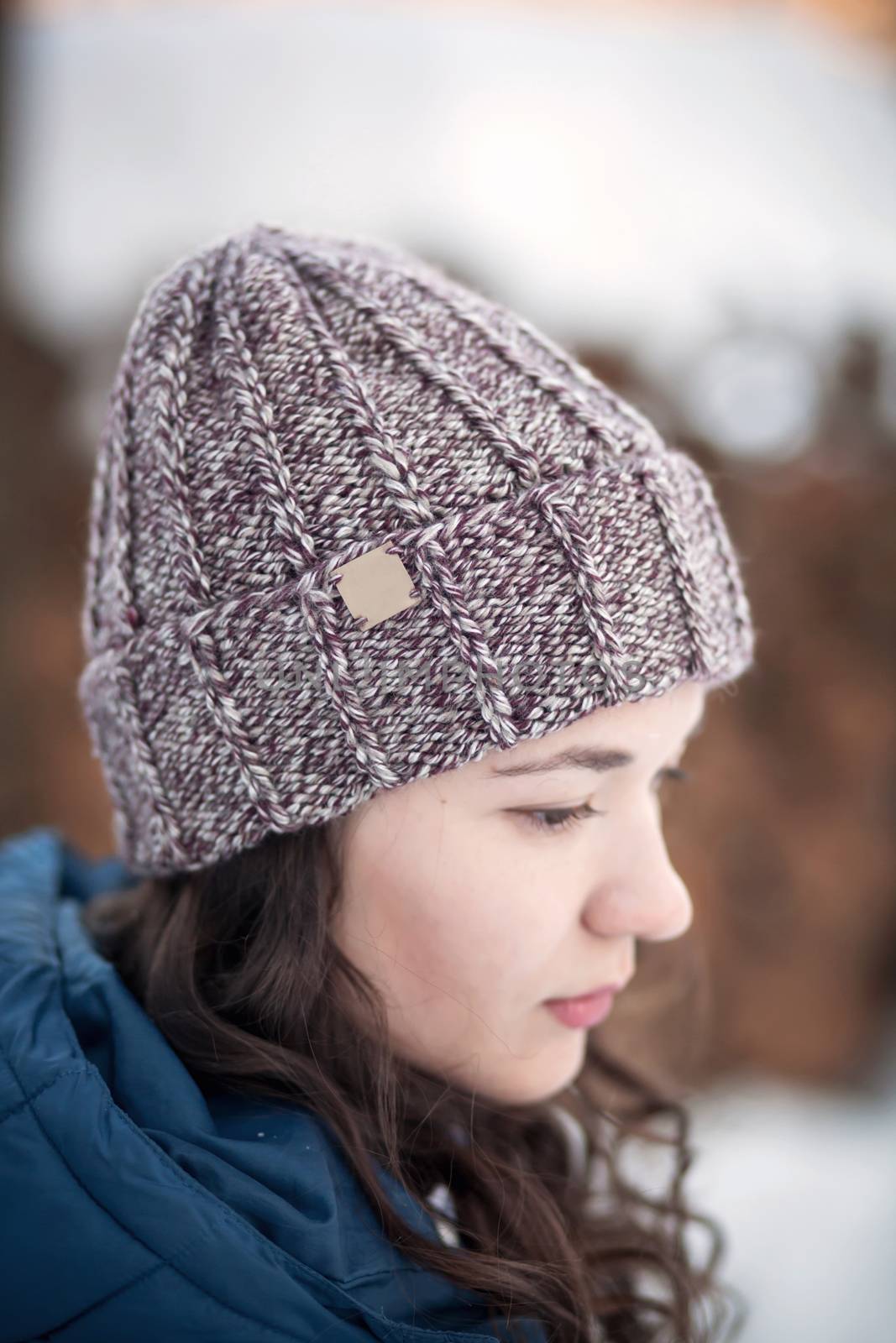 the beautiful young girl in a warm cap from wool of the alpaca in the winter forest. knitting