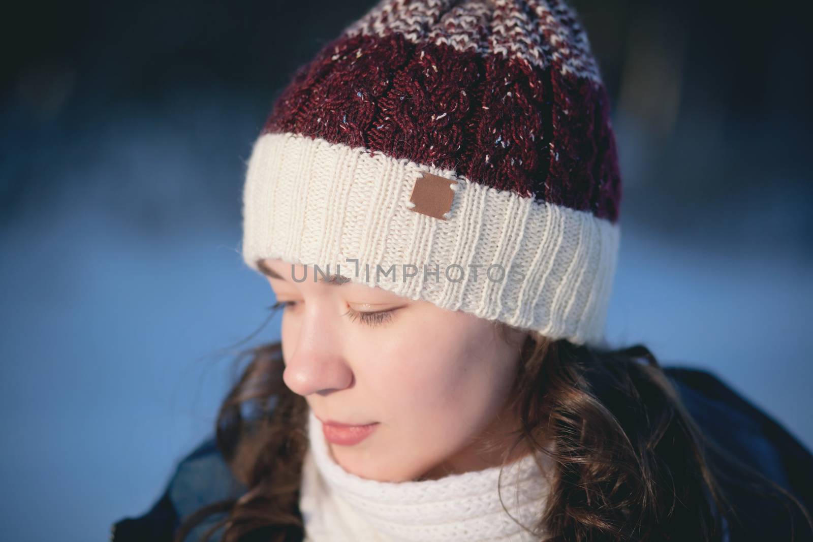 the beautiful young girl in a warm cap from wool of the alpaca in the winter forest. knitting