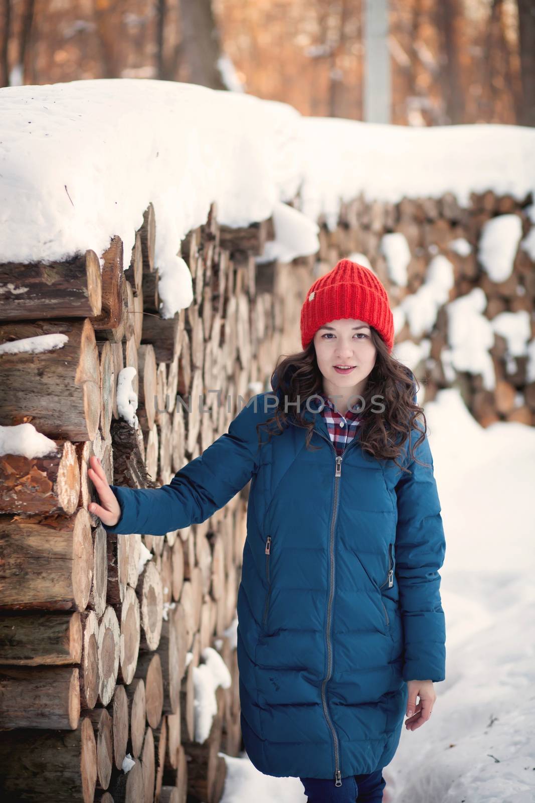the beautiful young girl in a warm cap from wool of the alpaca in the winter forest by polyats