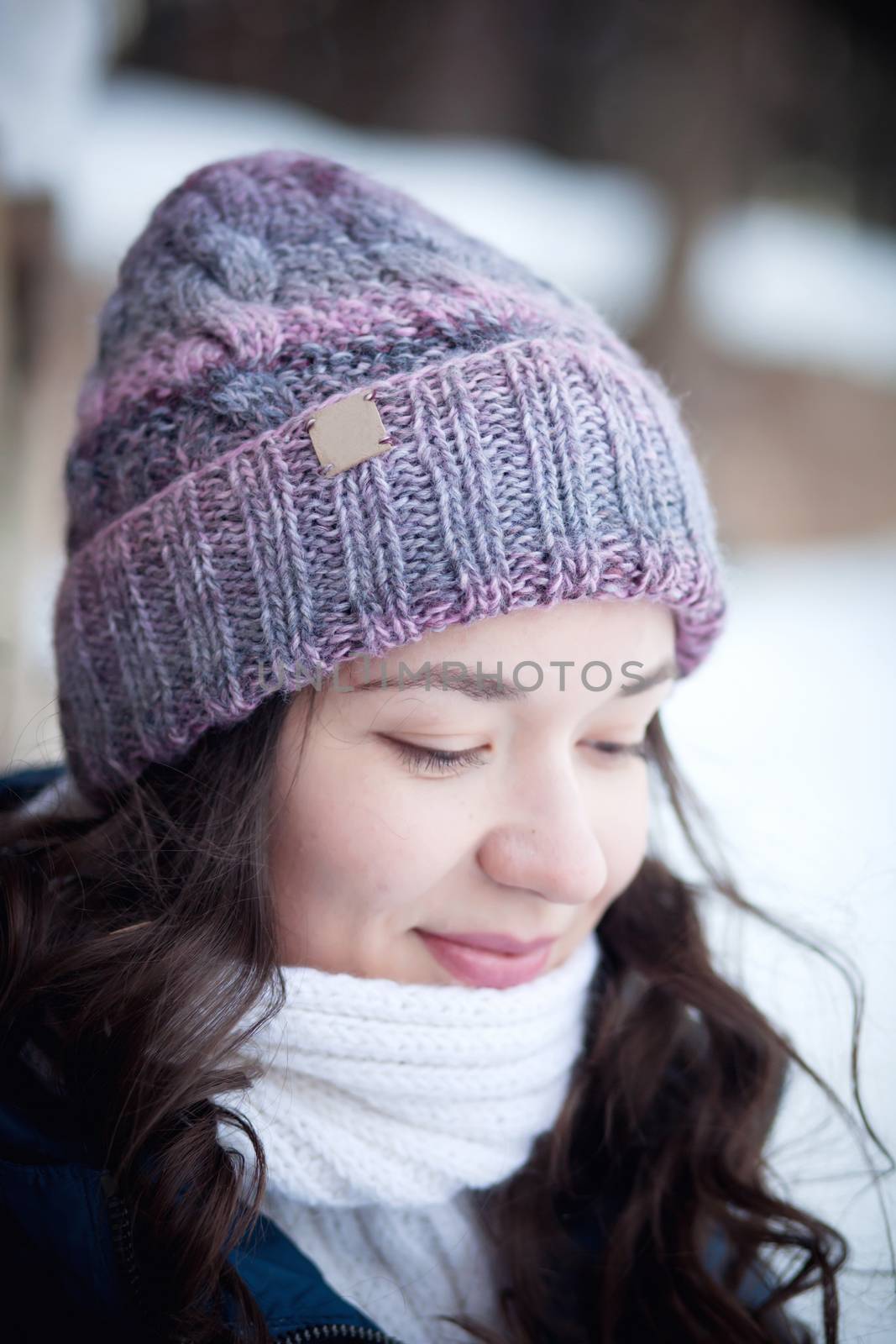 the beautiful young girl in a warm cap from wool of the alpaca in the winter forest by polyats