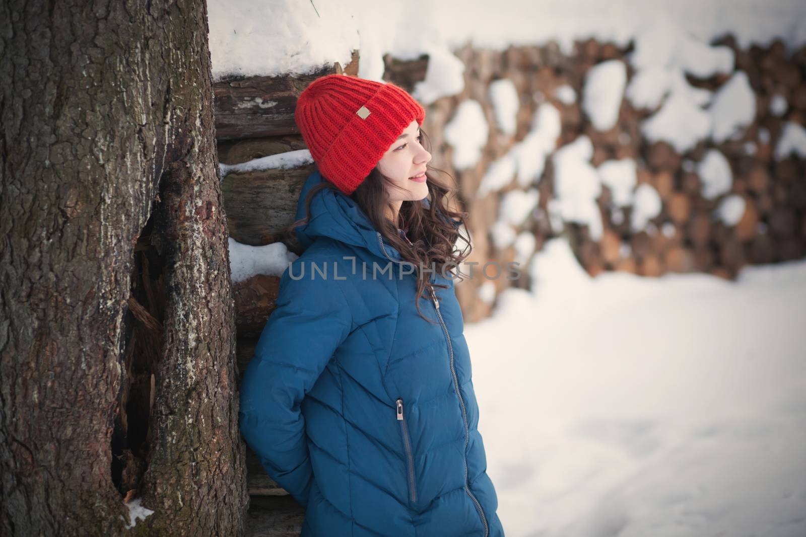 the beautiful young girl in a warm cap from wool of the alpaca in the winter forest by polyats