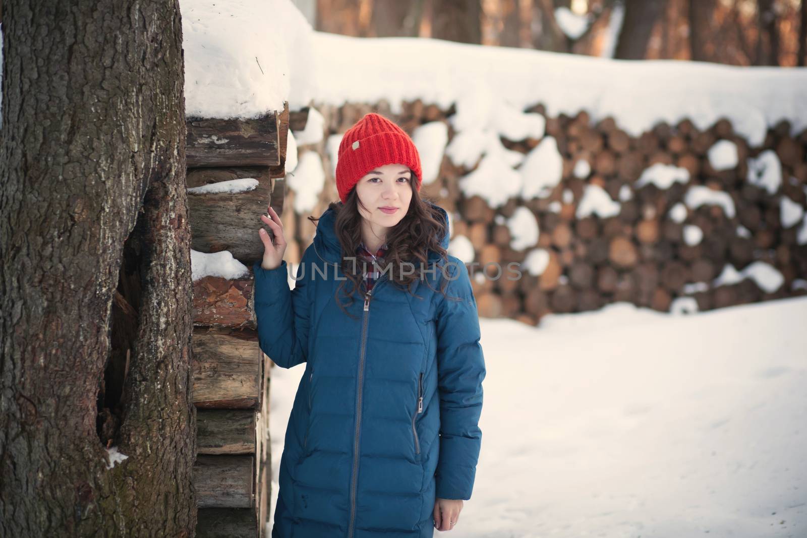 the beautiful young girl in a warm cap from wool of the alpaca in the winter forest by polyats