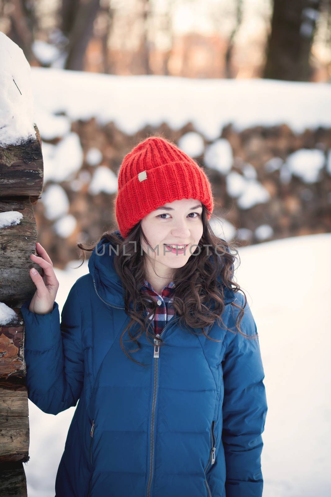 the beautiful young girl in a warm cap from wool of the alpaca in the winter forest by polyats