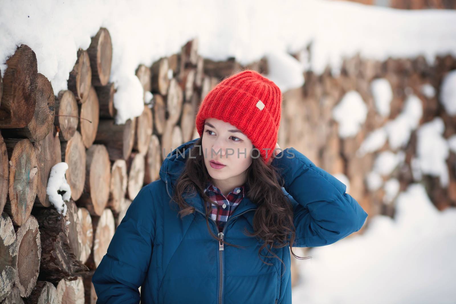 the beautiful young girl in a warm cap from wool of the alpaca in the winter forest by polyats