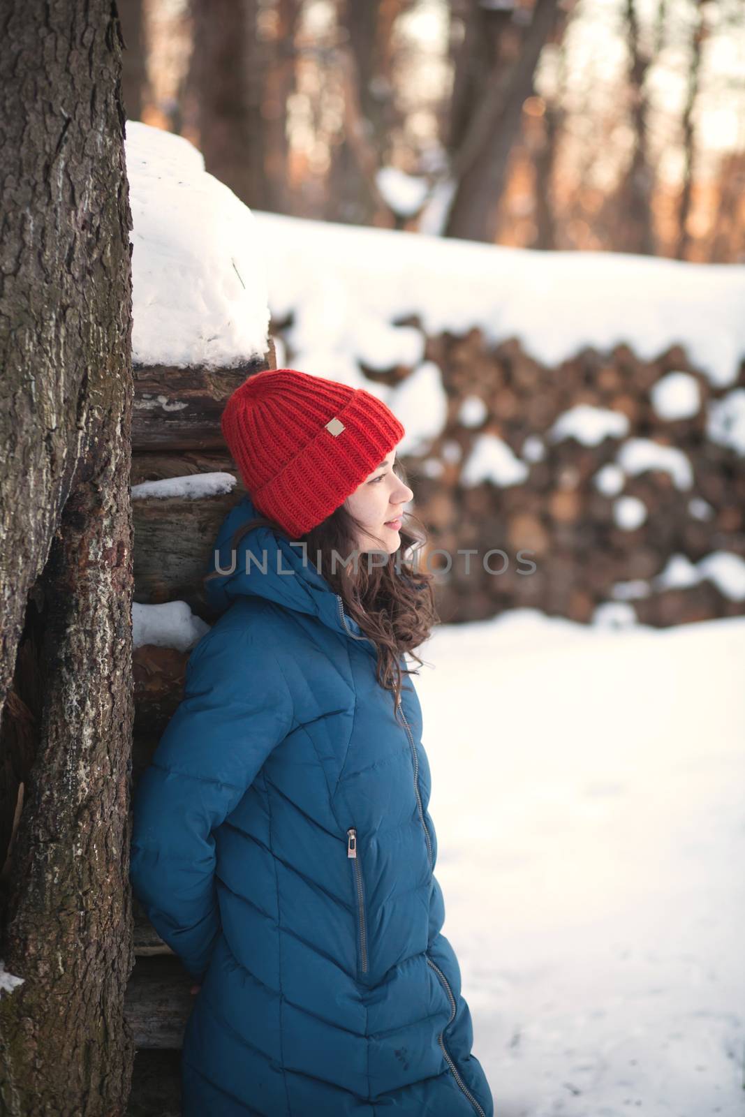 the beautiful young girl in a warm cap from wool of the alpaca in the winter forest by polyats