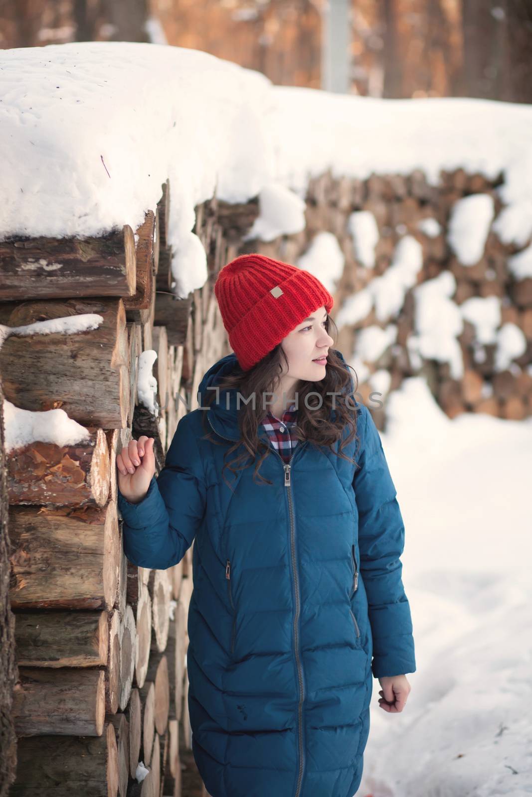 the beautiful young girl in a warm cap from wool of the alpaca in the winter forest by polyats