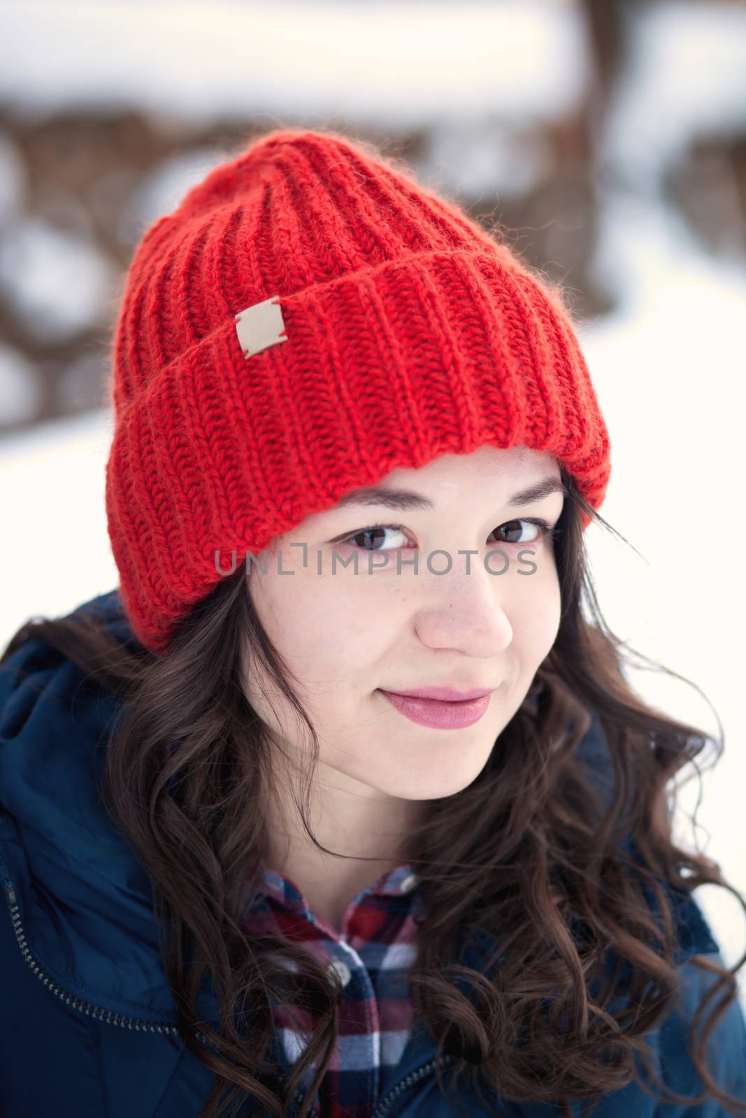 the beautiful young girl in a warm cap from wool of the alpaca in the winter forest by polyats