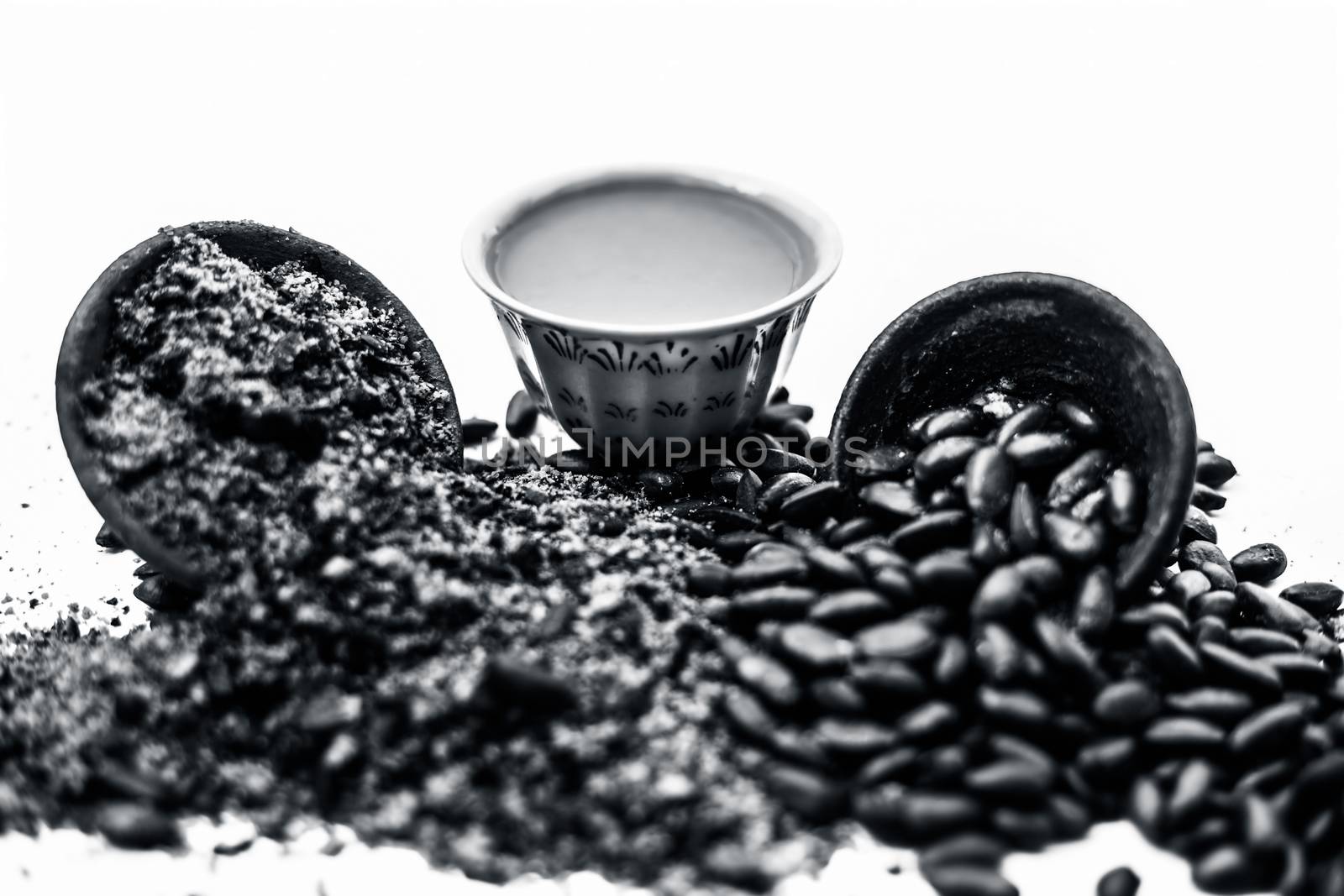 Close up of paste of custard apple seeds in a glass bowl with some powdered seeds and raw dried seeds isolated on white.