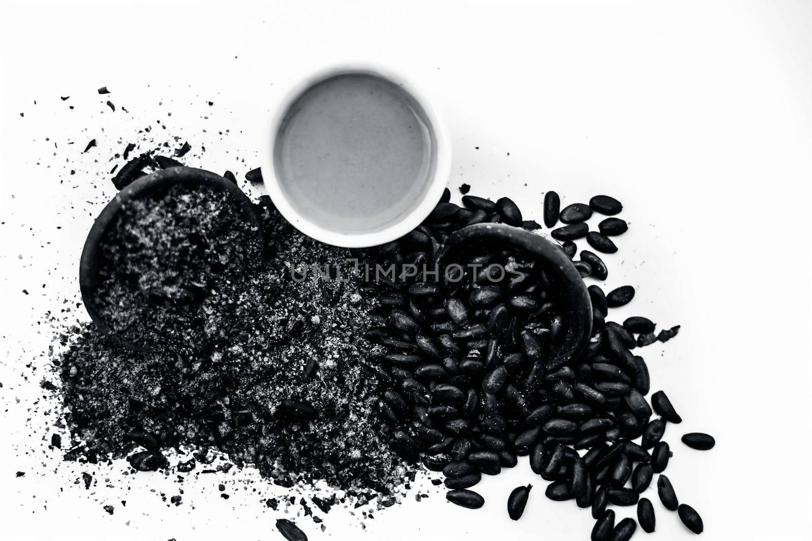 Close up of paste of custard apple seeds in a glass bowl with some powdered seeds and raw dried seeds isolated on white.