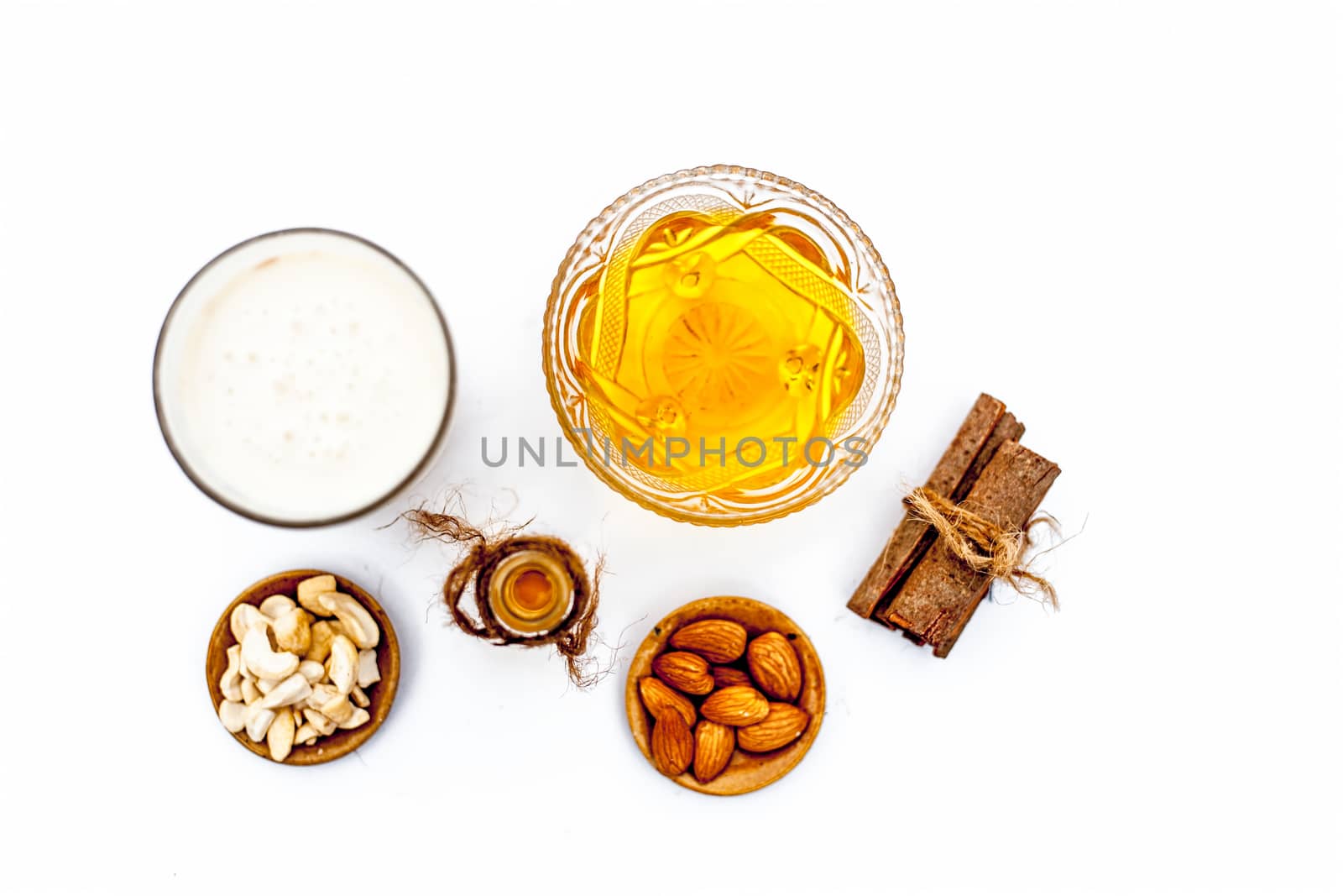 Close up of popular Indian & Asian winter drink isolated on white i.e Honey milk or shahad ka dudh in a transparent glass with entire ingredients which are milk,honey, and dry fruits.