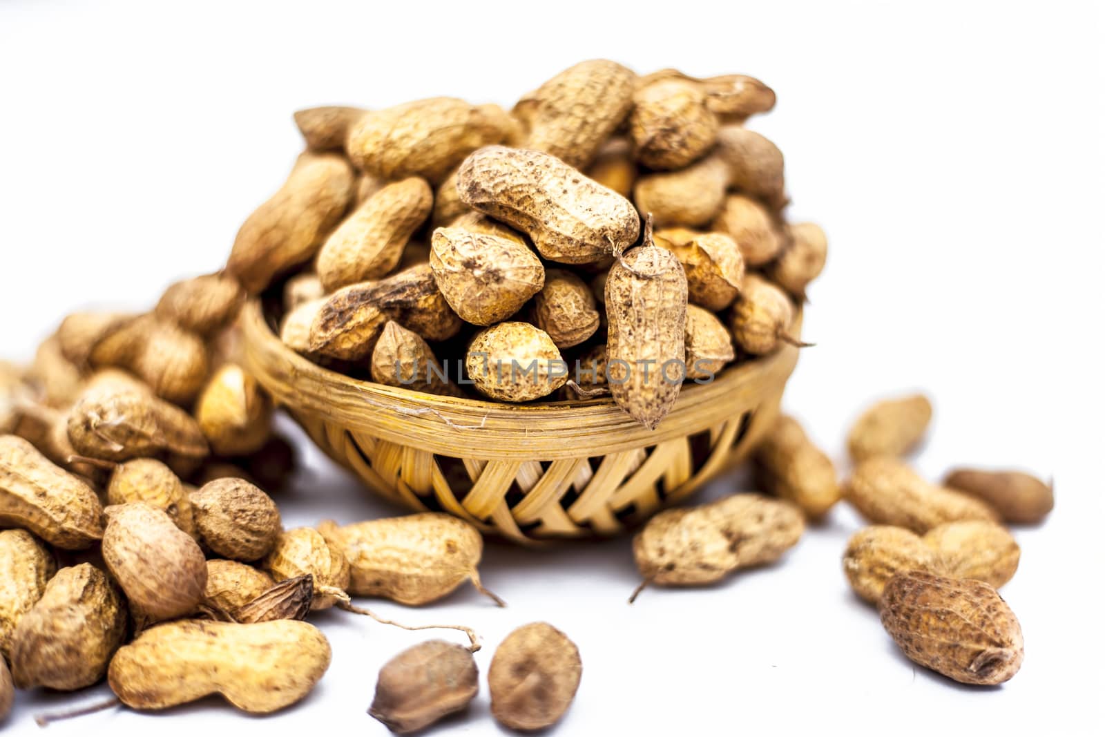 Close up of brown colored hamper having groundnuts or peanuts or moongaphalee or Arachis hypogaea or goober or monkey nut isolated on white. by mirzamlk