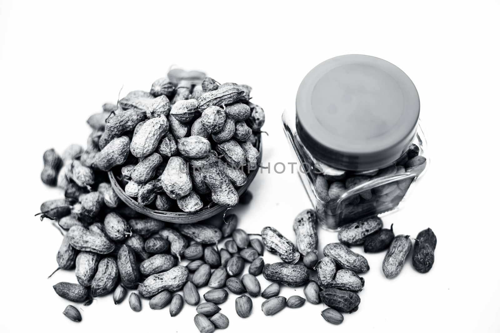 Close up of raw peanuts or groundnut isolated on white with some peeled in a separate bottle.