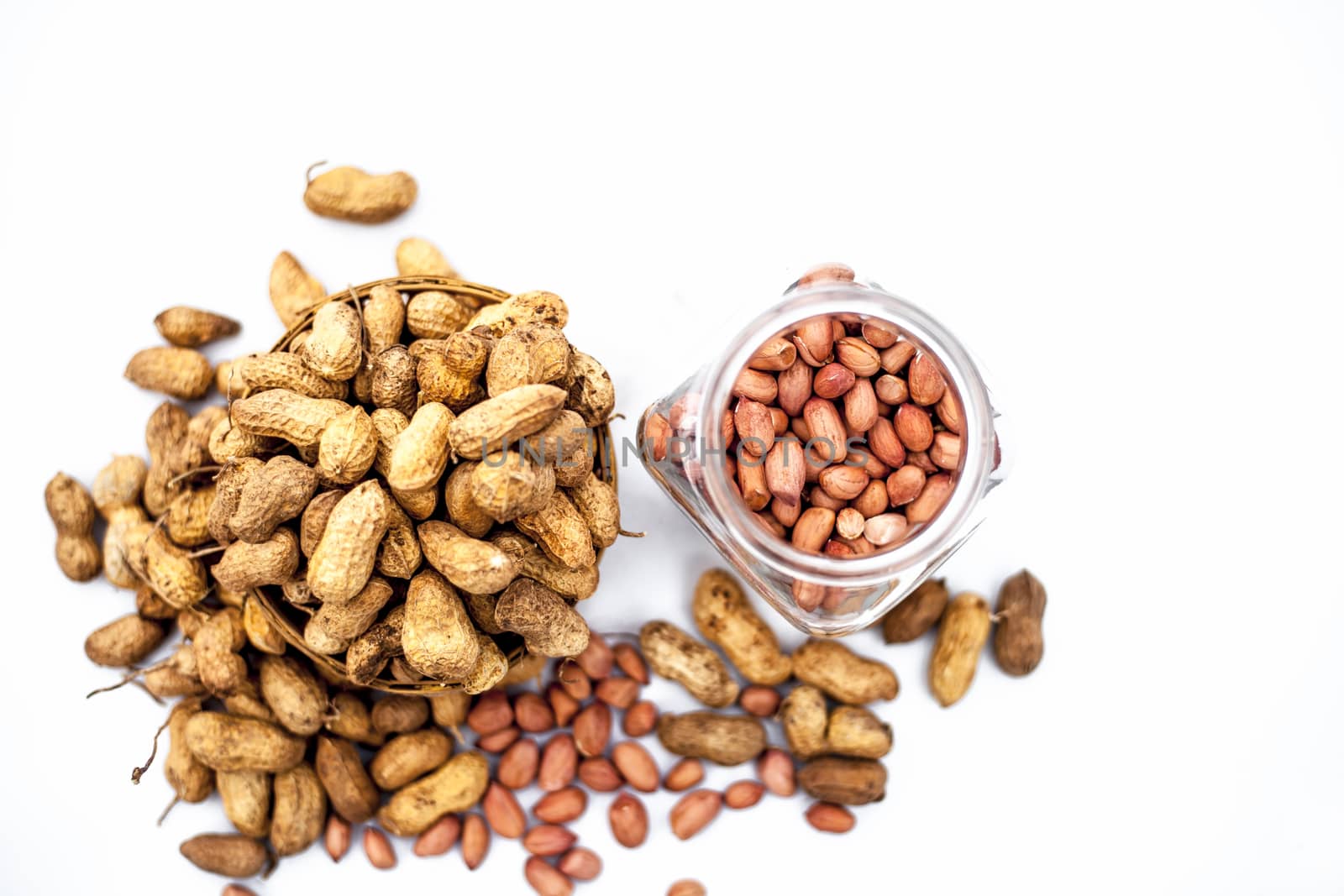 Close up of raw peanuts or groundnut isolated on white with some peeled in a separate bottle.