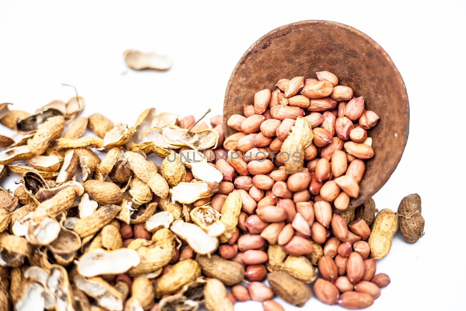 Raw organic groundnut or peanuts isolated on white with raw peanuts in a hamper with peanuts in clay bowl.