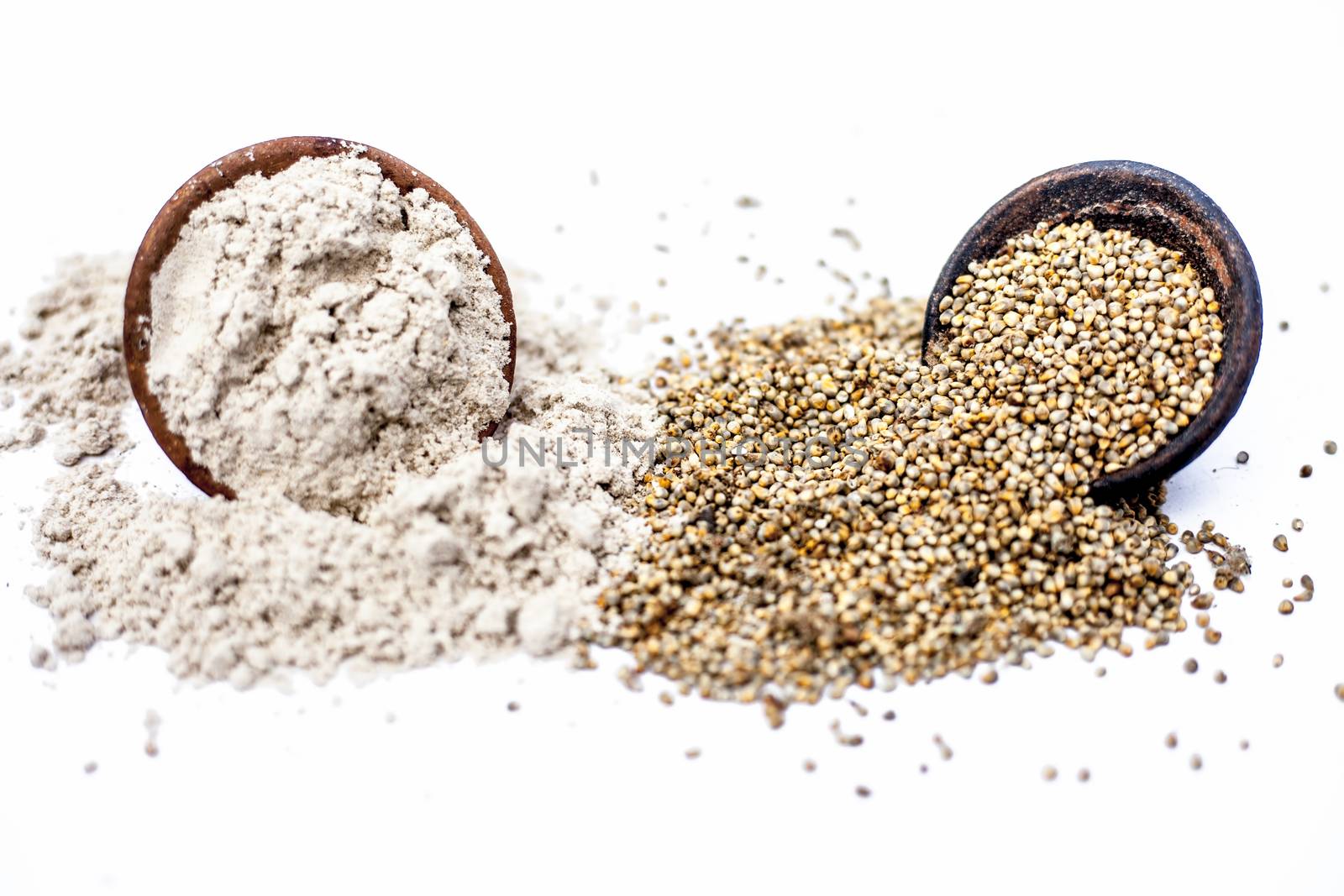 Close up of flour of pearl millet or bajra in a clay bowl with raw pearl millet in a clay bowl isolated on white.