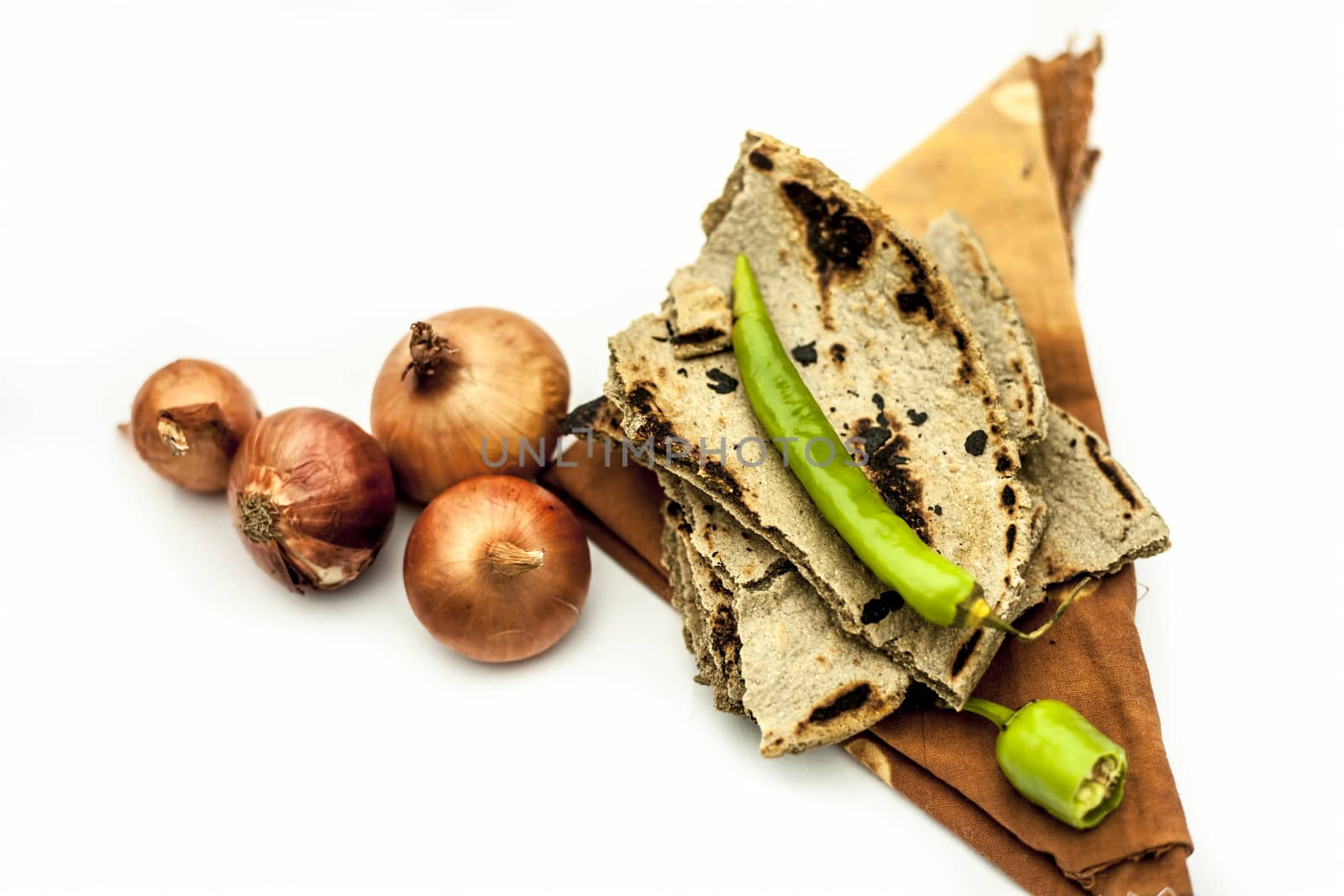 Poor man's lunch or farmer's lunch isolated on white or common items eaten in lunch isolated on white which are bajri ki roti with cut and raw onion along with green chili.