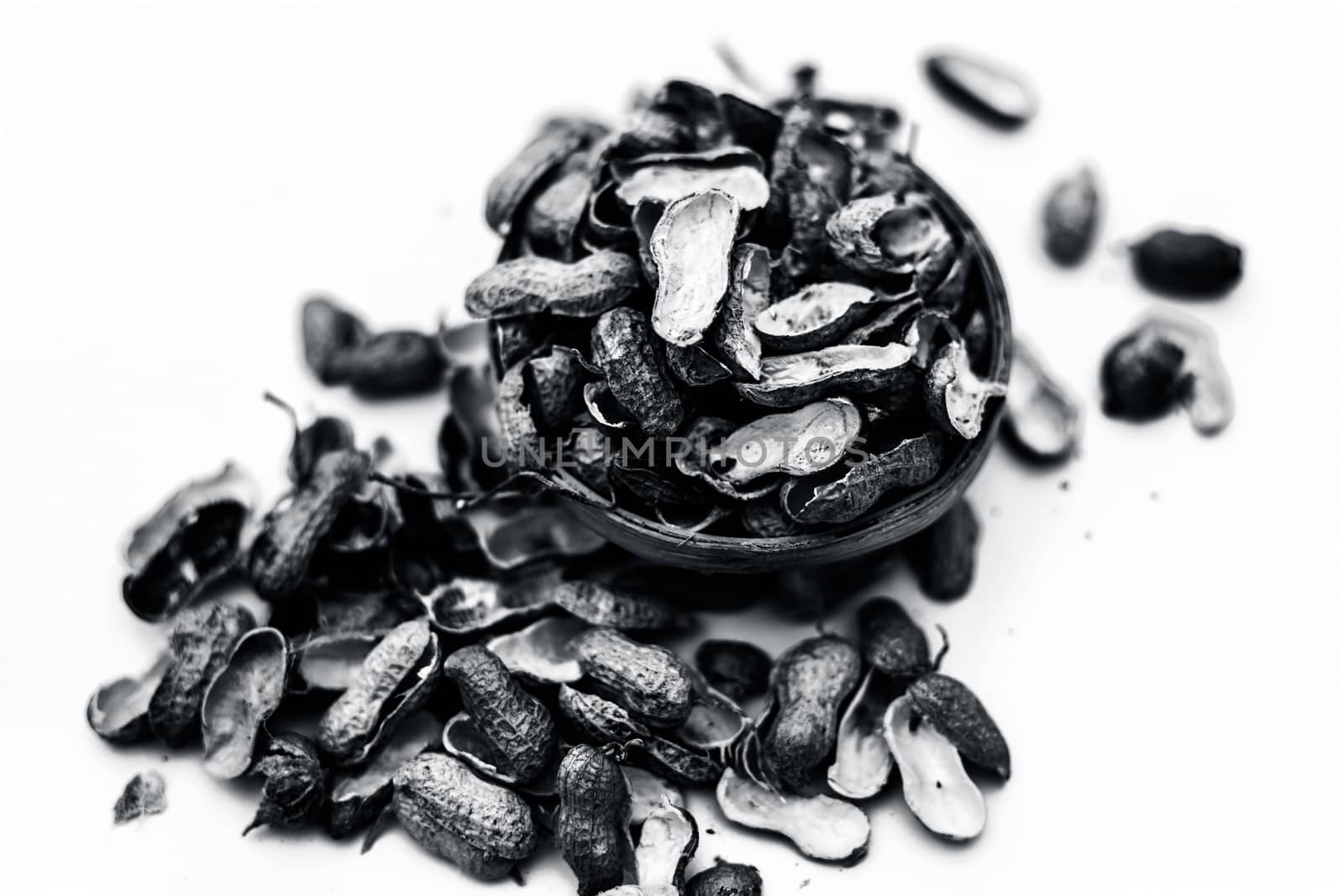 Close up of brown colored hamper having groundnuts or peanuts or moongaphalee or Arachis hypogaea or goober or monkey nut some in shells and some opened isolated on white.