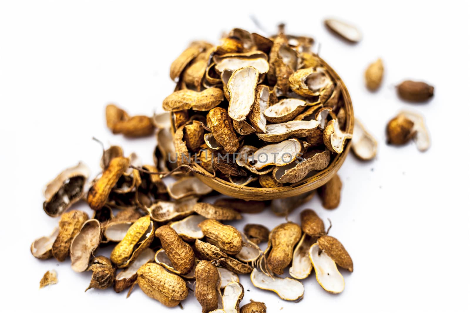 Close up of brown colored hamper having groundnuts or peanuts or moongaphalee or Arachis hypogaea or goober or monkey nut some in shells and some opened isolated on white.