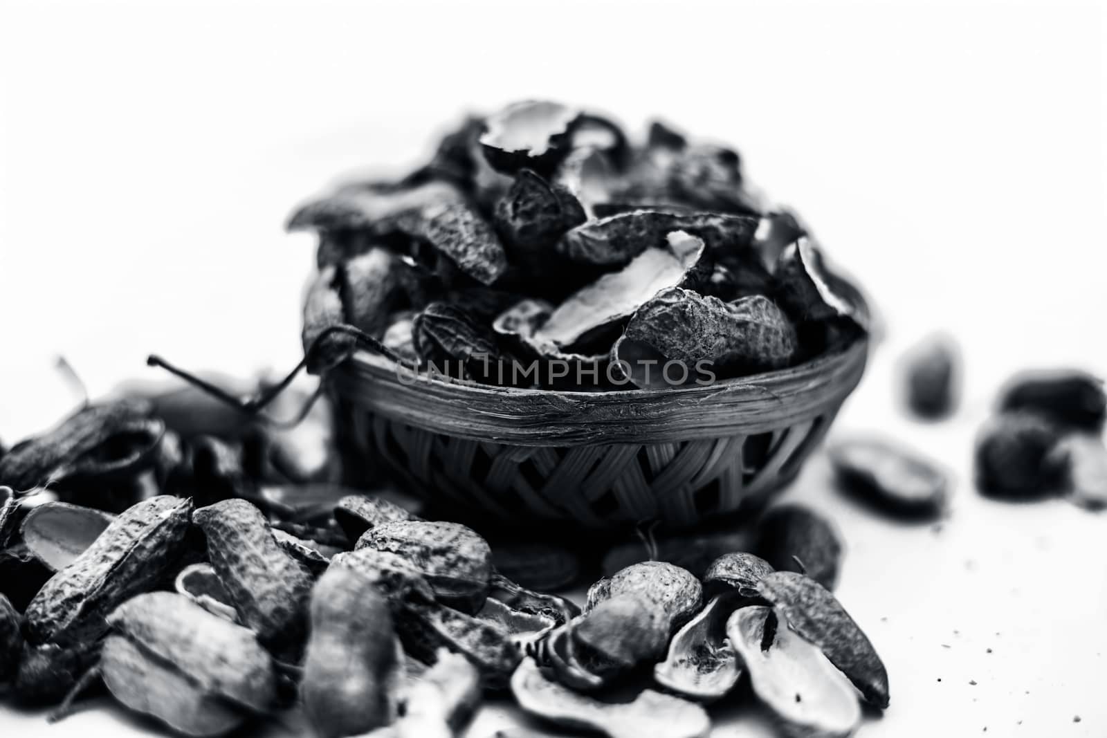 Close up of brown colored hamper having groundnuts or peanuts or moongaphalee or Arachis hypogaea or goober or monkey nut some in shells and some opened isolated on white.