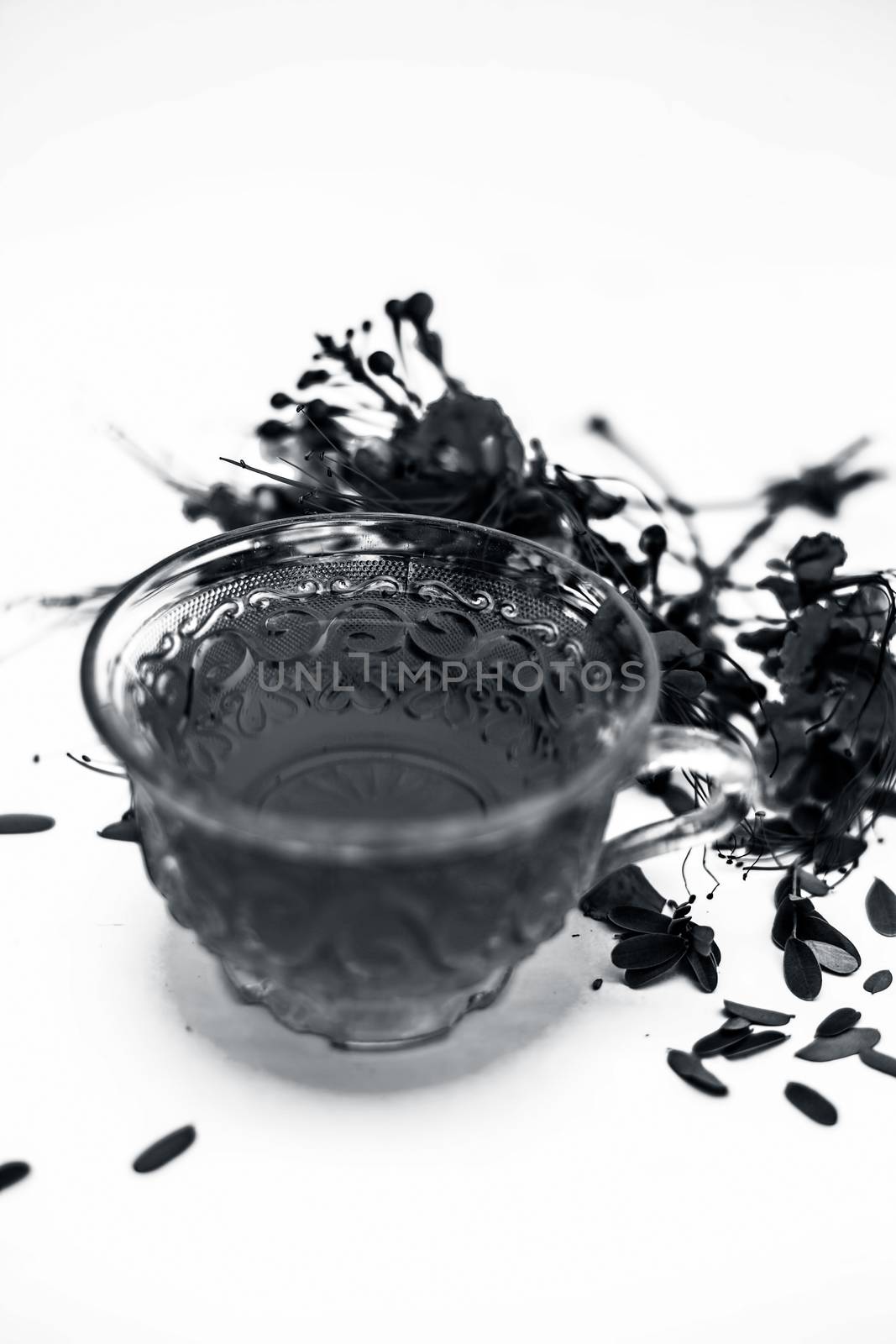 Close up of orange colored herbal floral tea of peacock flower or Caesalpinia pulcherrima in a transparent cup along with raw flower isolated on white.