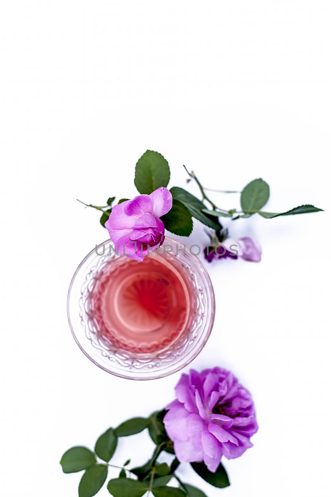 Close up view of organic fresh rose tea in a transparent glass cup isolated on white with raw roses.