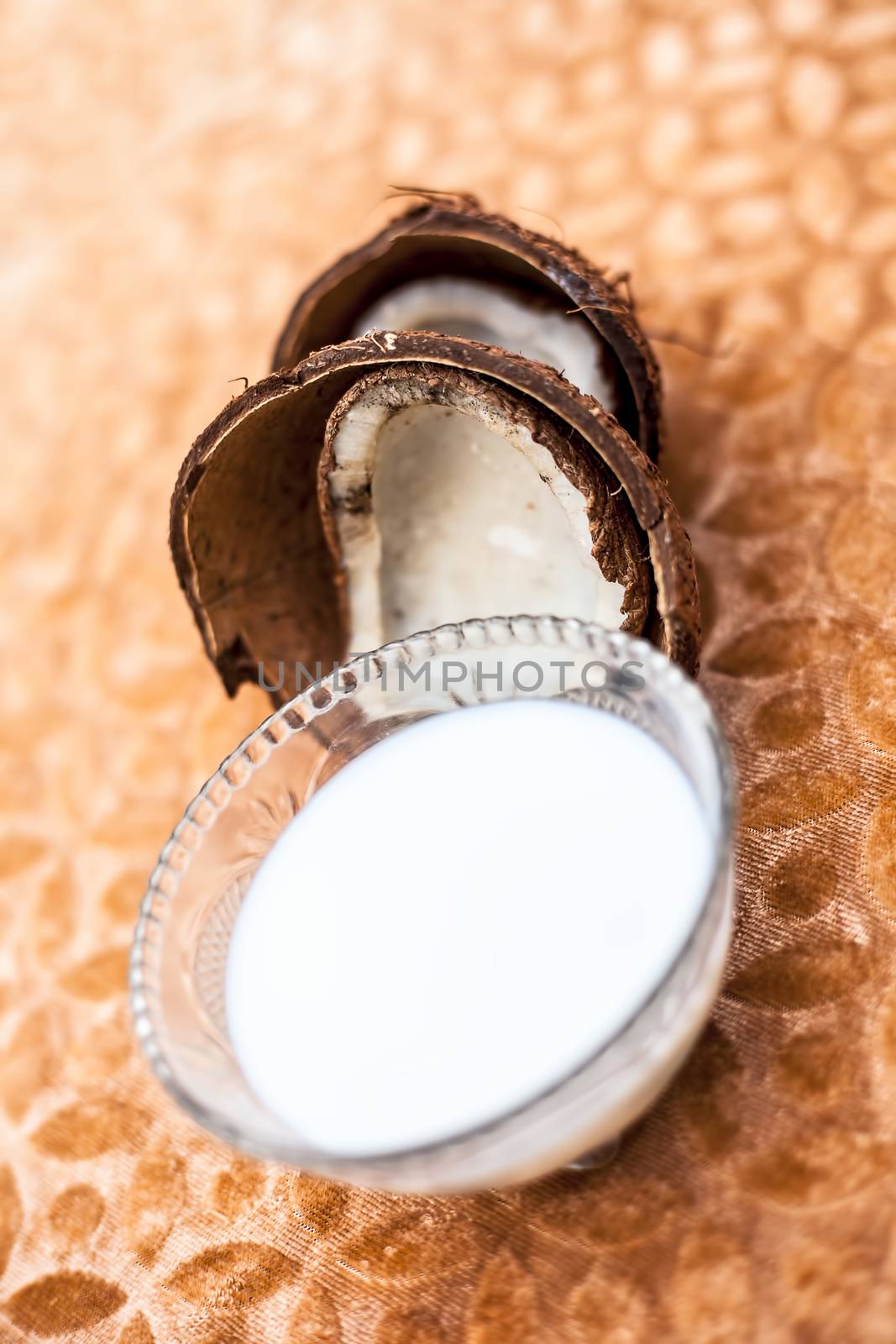 Close up of organic fresh coconut milk in a glass bowl with raw dried coconut isolated on brown colored surface.