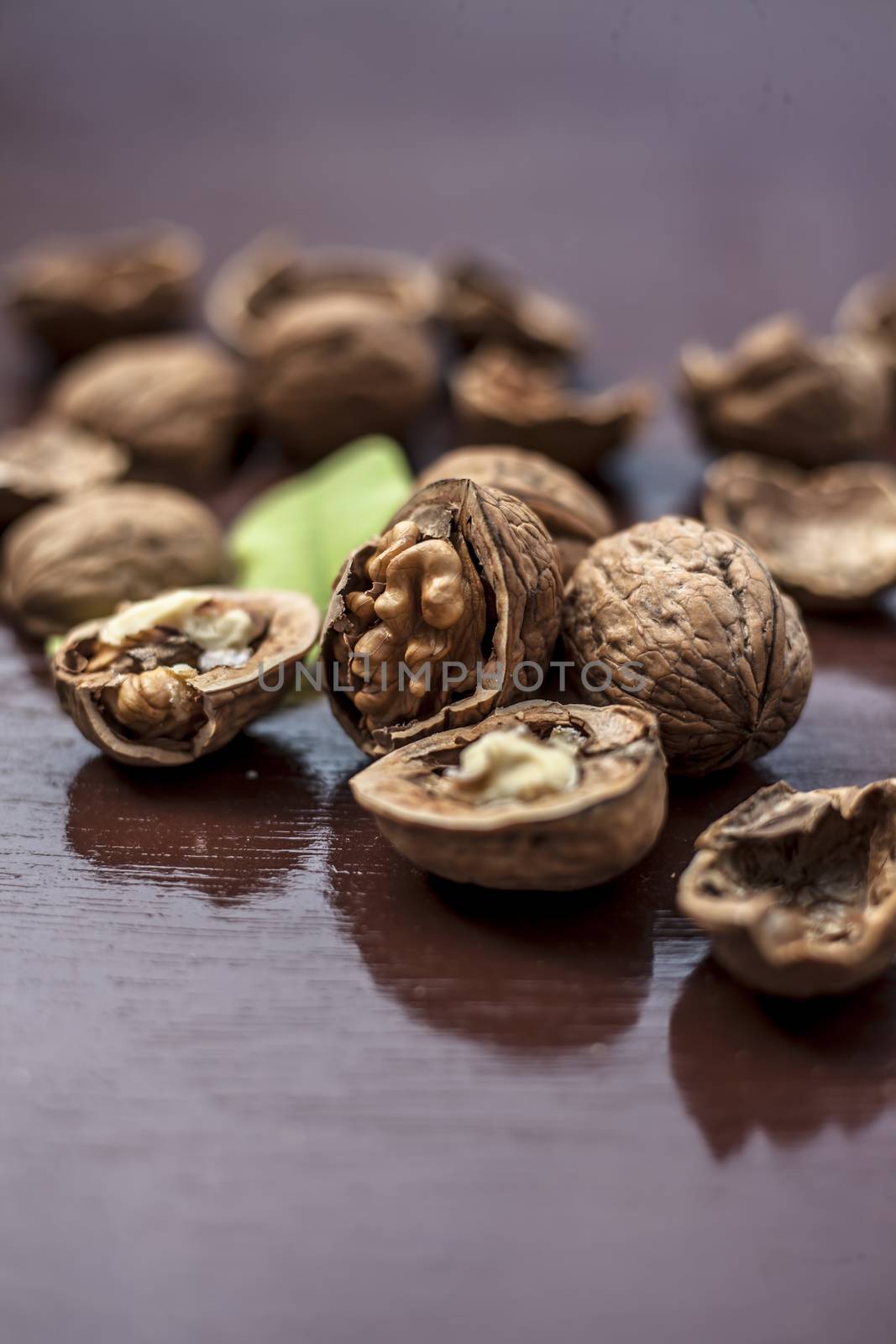 Close up of walnuts in shell and some broken on brown colored wooden surface.