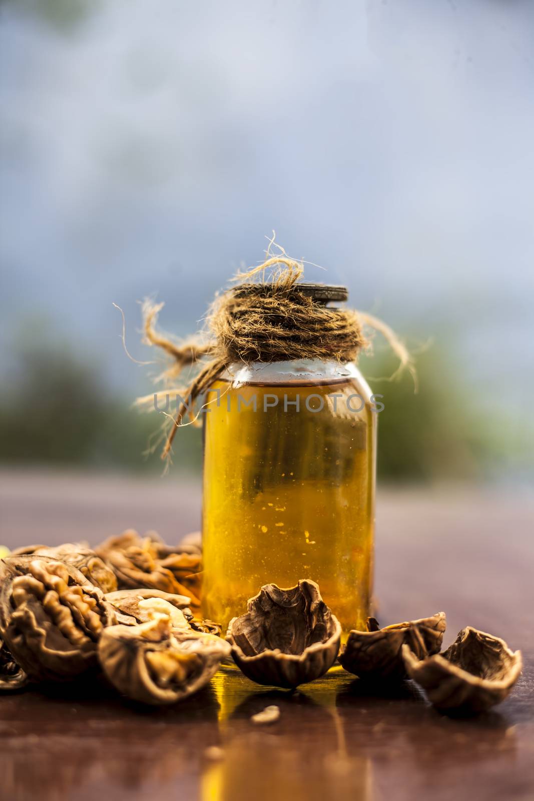 Close up of herbal organic extracted walnut oil in a transparent glass bottle with raw wall nuts on wooden surface.