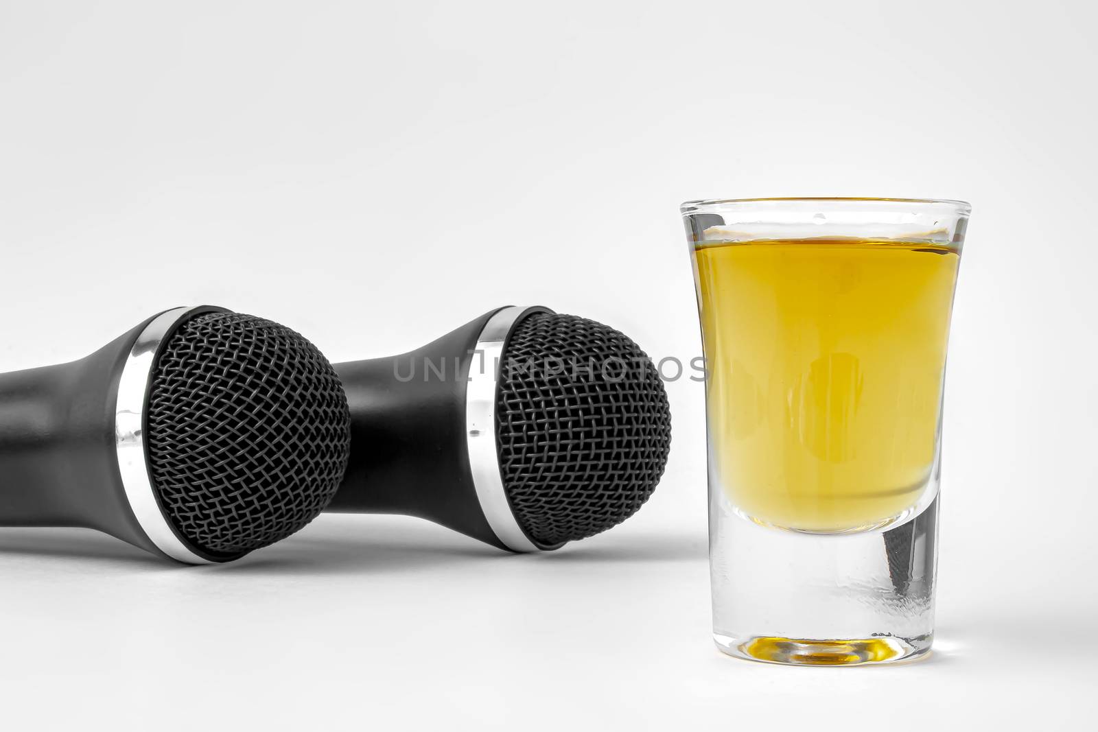A shoot glass with liquor and two karaoke microphones on a white background