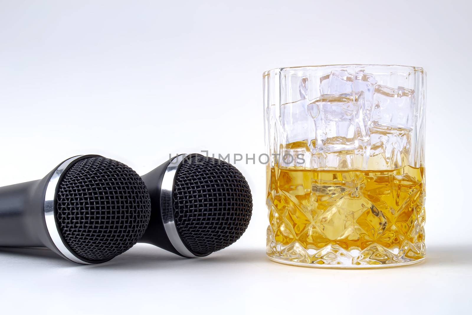 A whisky glass with ice and liquor and two karaoke microphones on a white background by oasisamuel