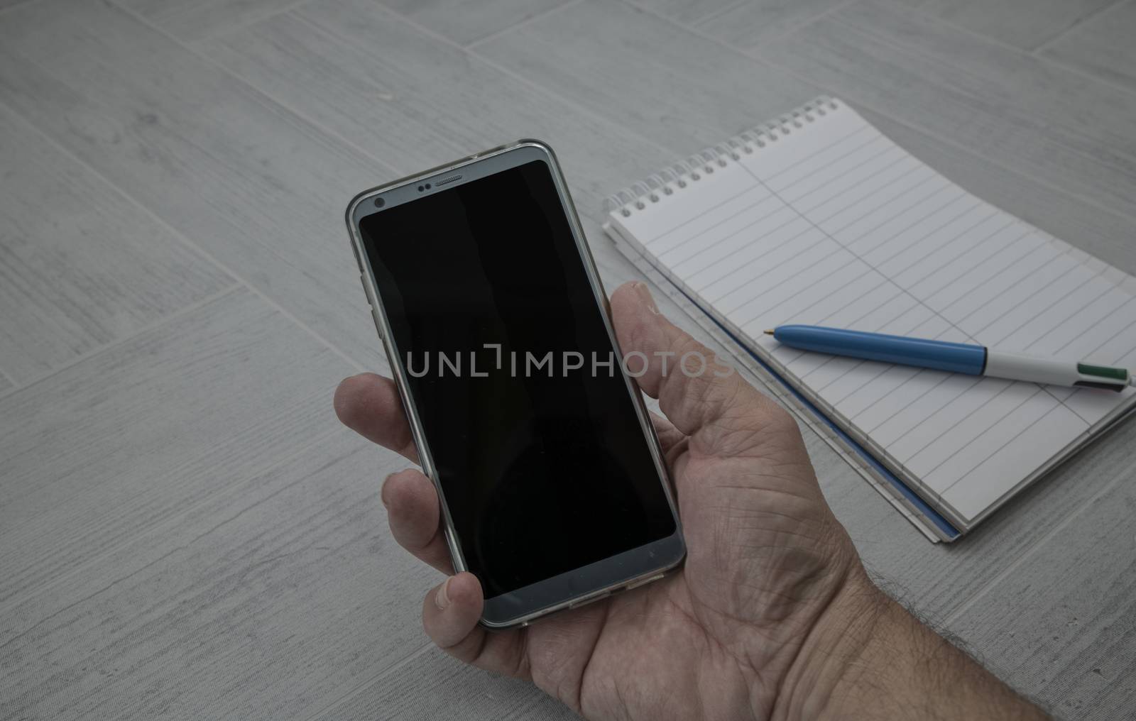 male hand holding mobile phone with paperwork and pen as background