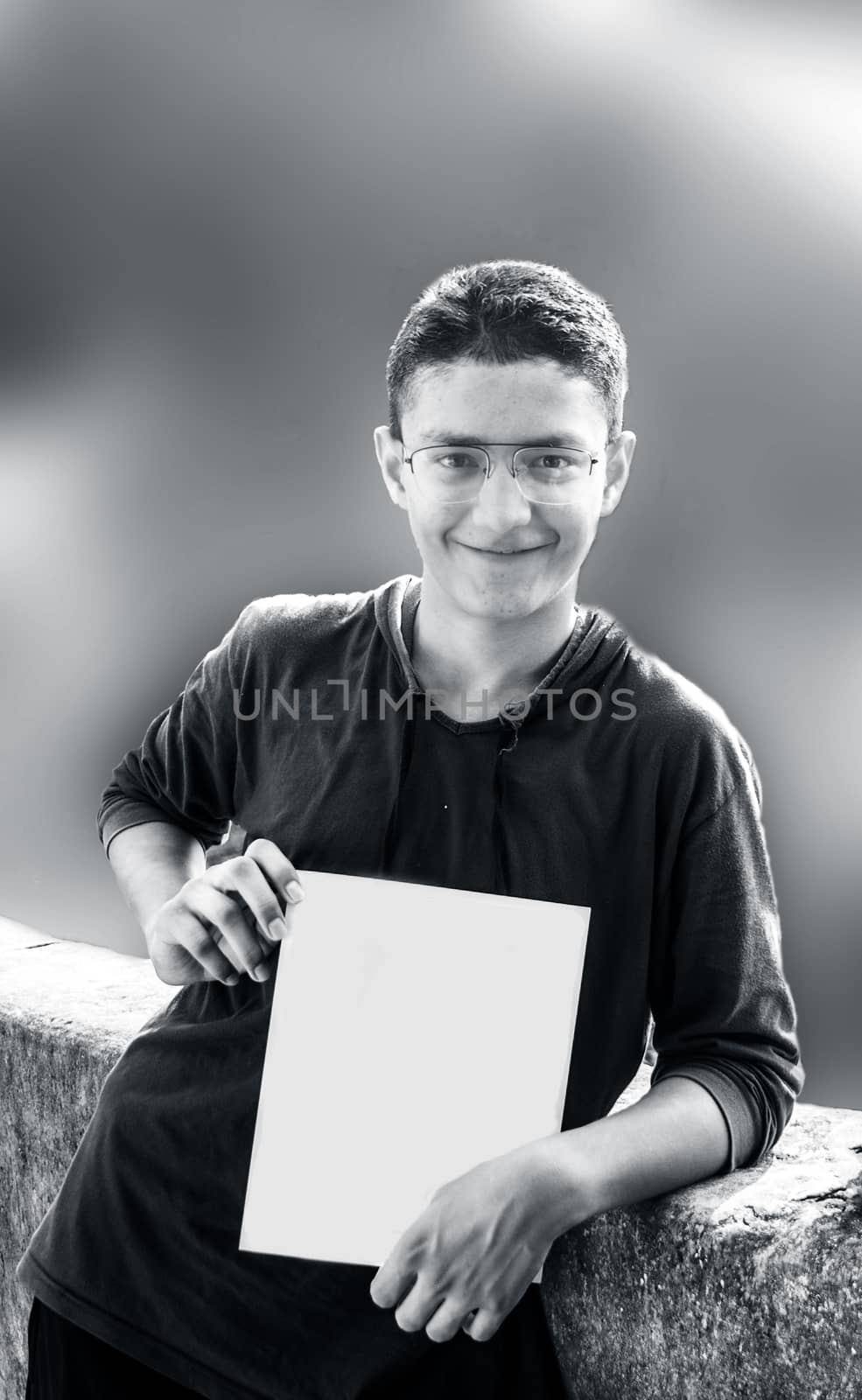 Portrait of a youngster with green color t-shirt and spectacles and holding a blank sheet,smiling and starring at the camera.