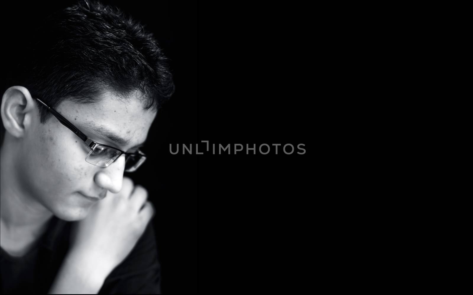 Portrait of young teenager boy wearing half rim black colored reading glass or spectacles and a green hooded T-shirt posing in black dark background.Low key portrait. by mirzamlk