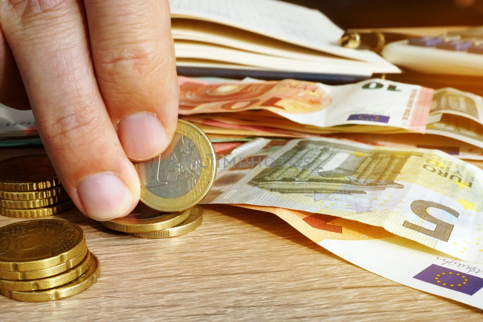 Man is holding euro coin and banknotes on a desk. Savings.