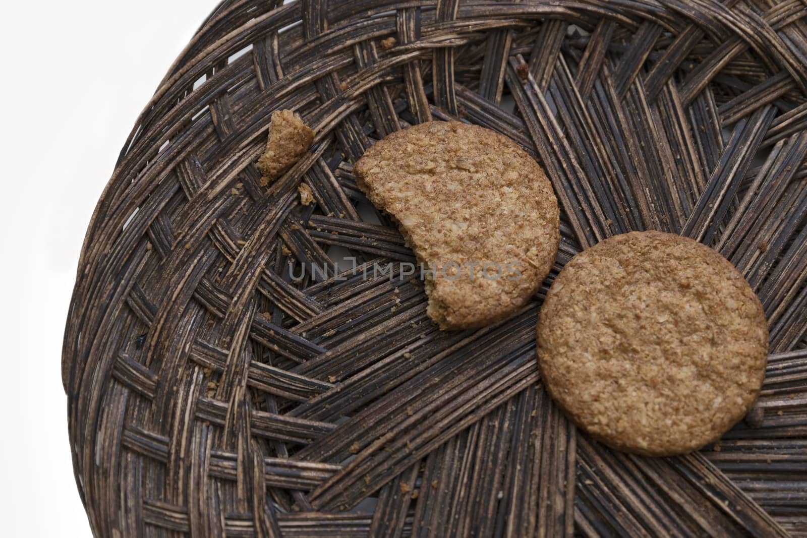 Close-up of two oatmeal cookies on a brown wicker plate on a white background