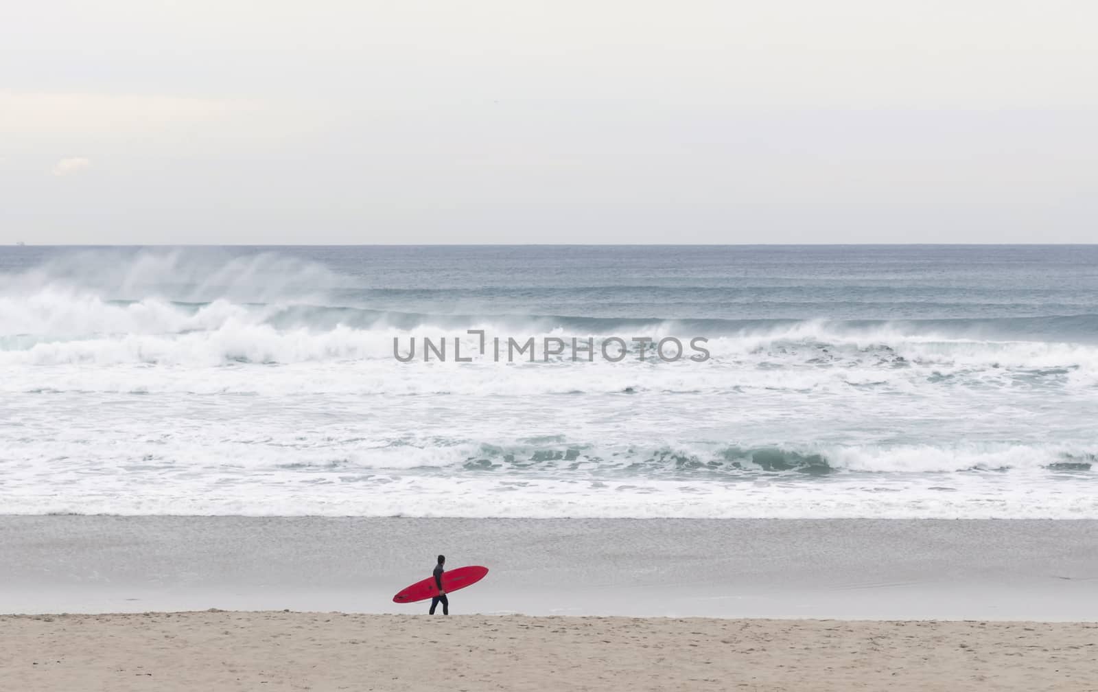 Red board surfer walking on the beach with waves in the background