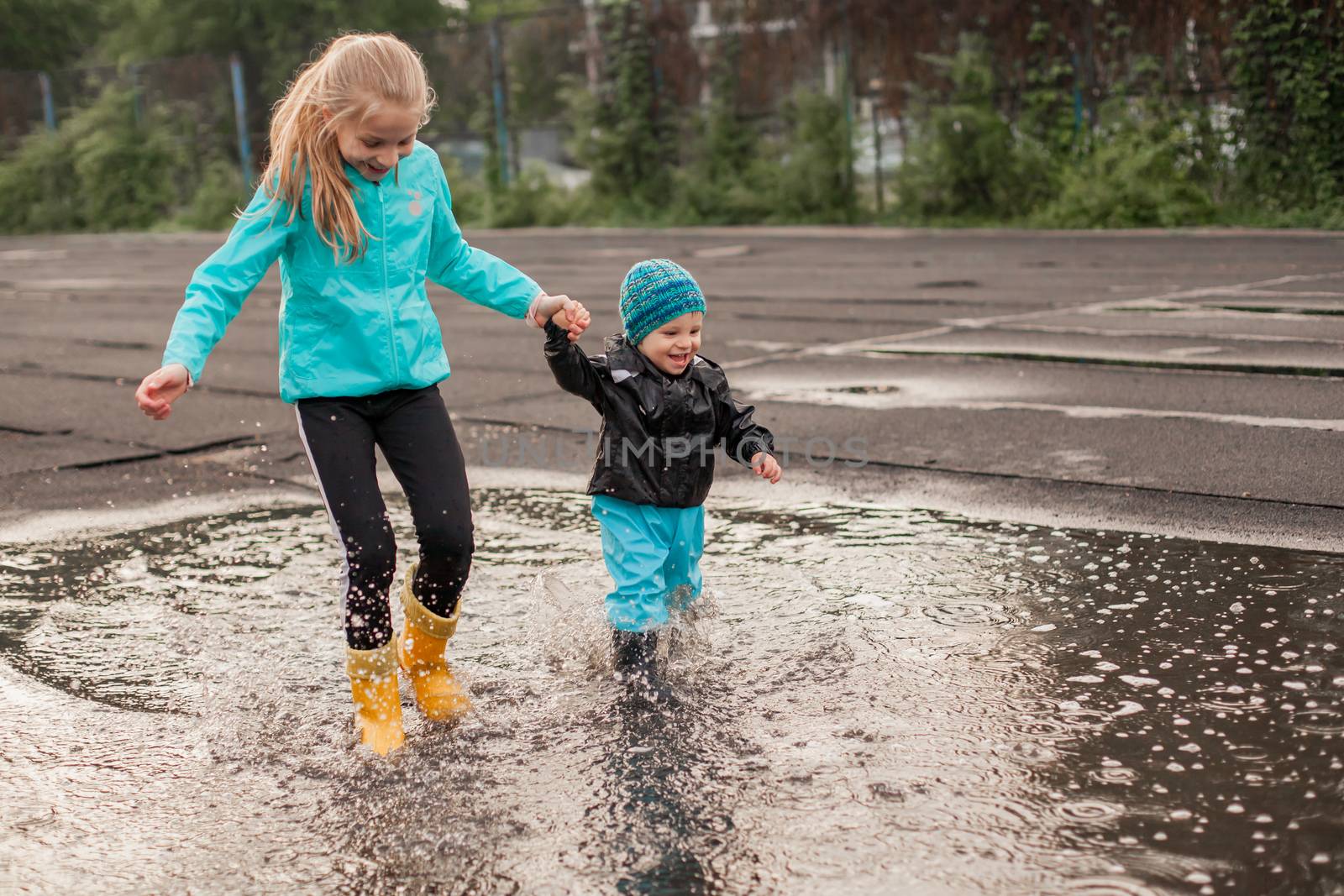 Boy and girl jumping in puddle in waterproof coat and rubber boots