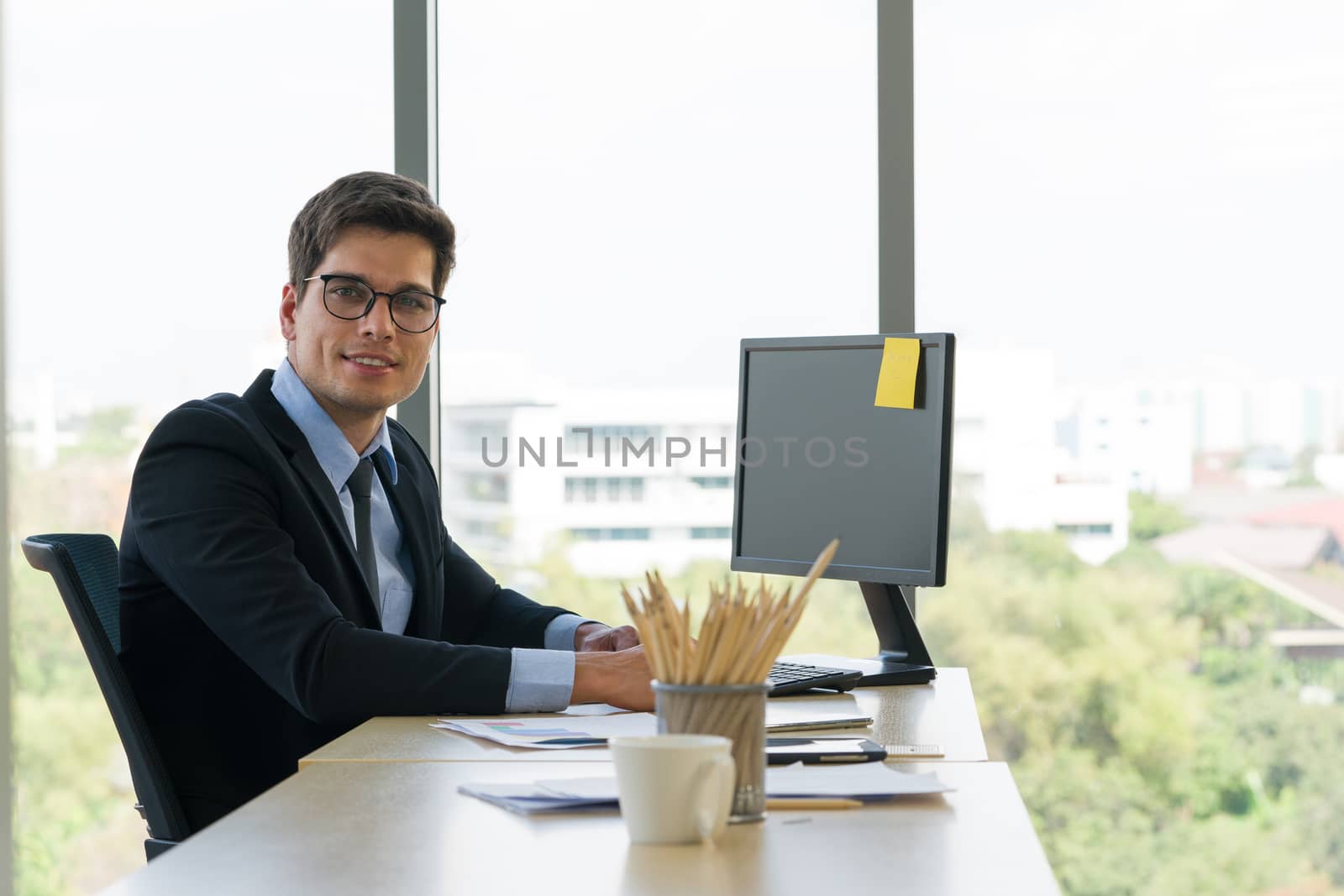A young business man in a dark suit smiled happily after seeing the note on his computer screen. Morning work atmosphere In a modern office.
