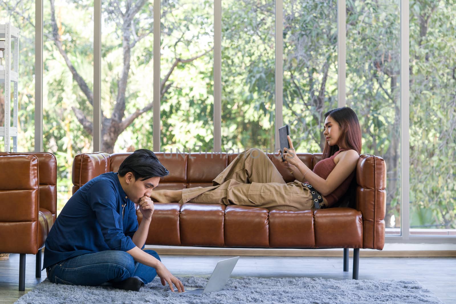 Young lovers spend time together on holidays in the living room. The man wore comfortable clothes use laptop computer to search for jobs. The girl is checking email using a tablet computer.