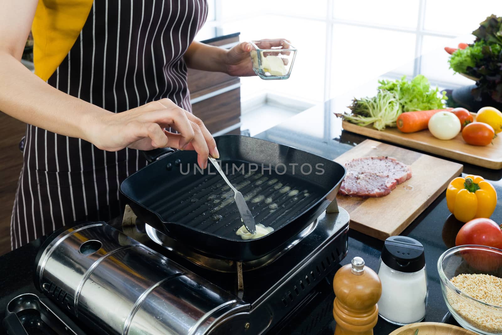 The housewife dressed in an apron putting butter in the pan prepared for frying steaks.