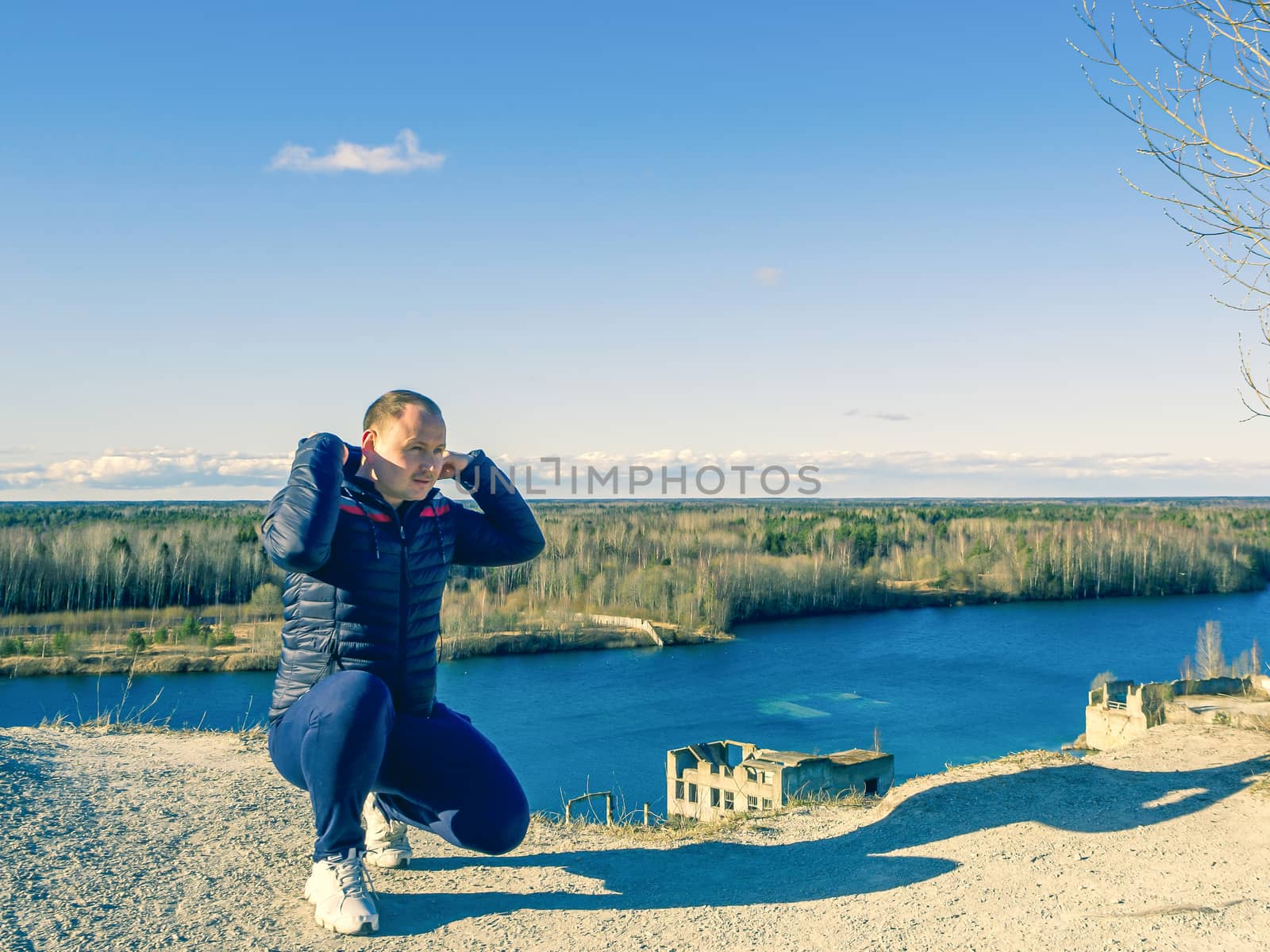 Man sitting on the pick of a mountain and looking into the distancee. Vantage point of Rummu quarry, Estonia. Clear blue sky. Travel concept. copy space