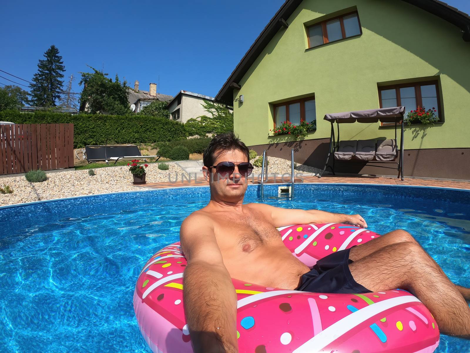 Happy man relax on inflatable ring in small home swimming pool. Covid 19, Summer Holiday 2020 holiday concept. Vacation at home or on garden.