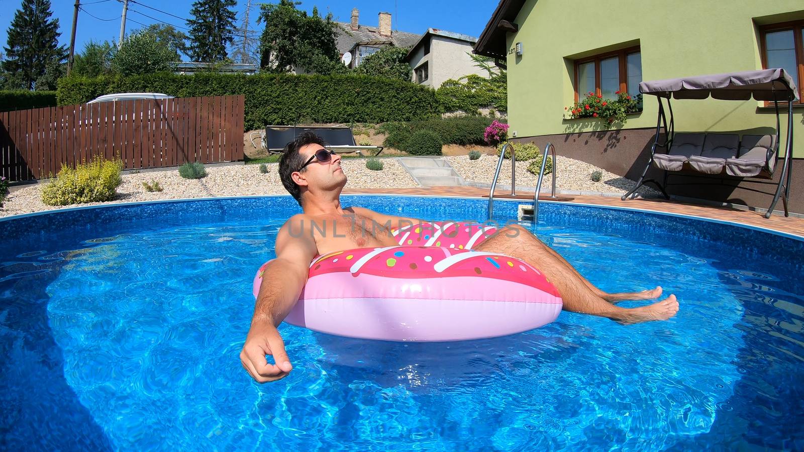 Happy man relax on inflatable ring in small home swimming pool. Covid 19, Summer Holiday 2020 holiday concept. Vacation at home or on garden.