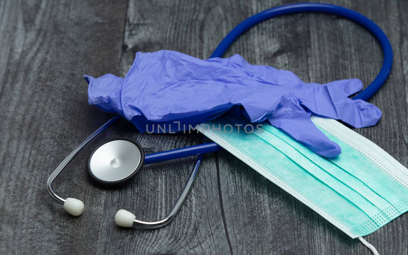 A pair of blue rubber medical gloves, surgical mask and blue stethoscope on a wooden table.